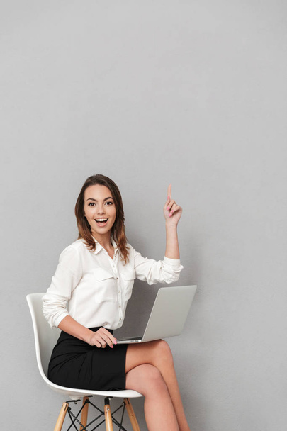 Photo of excited happy young business woman sitting isolated over grey wall background pointing using laptop computer. - Photo, image