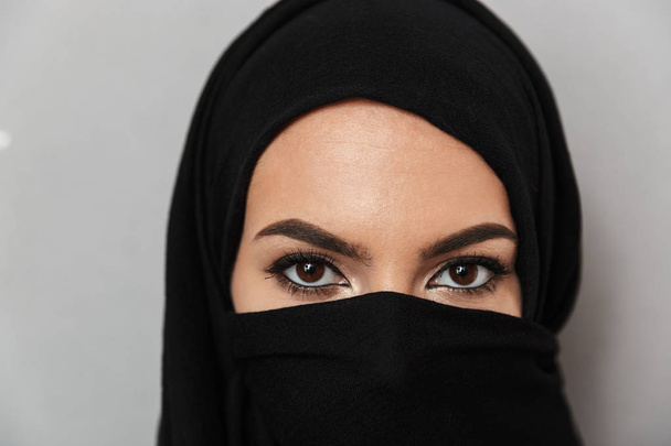 Close up portrait of a beautiful arabian woman wearing hijab looking at camera isolated over gray background - Фото, зображення
