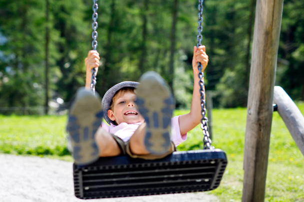 Funny kid boy having fun with chain swing on outdoor playground while being wet splashed with water - Photo, image