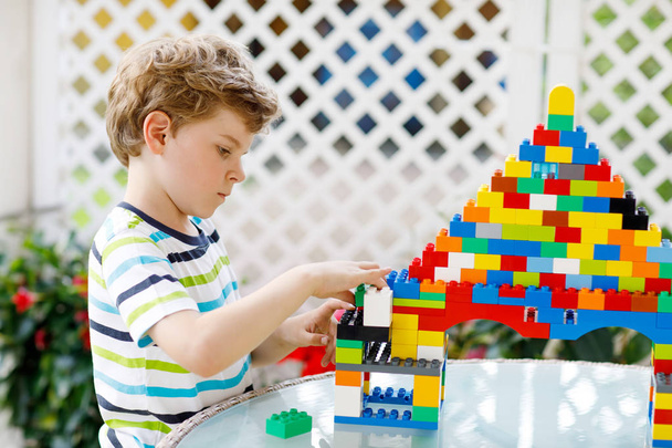 Little blond child and kid boy playing with lots of colorful plastic blocks. - Photo, Image