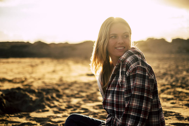 Lächeln nettes blondes Mädchen 25 Jahre alt bleiben am Strand sitzen, sich ausruhen und nach hinten schauen. goldener Sonnenuntergang im Hintergrund. Strand Natur Outdoor Freizeit Lifestyle - Foto, Bild