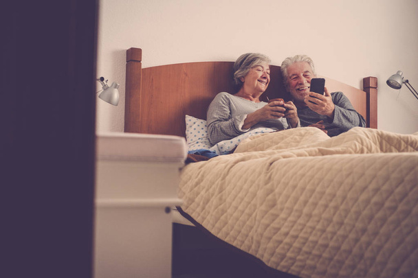 szép, gyönyörű modellek pár felnőtt idősebb 70 éves szórakoztunk, és élvezze az ágyban otthon, a hálószobában. reggel lusta ébrednek, nem sietnek, miközben brekfast e-maileket és a tartalmát a smartphone ellenőrzése - Fotó, kép