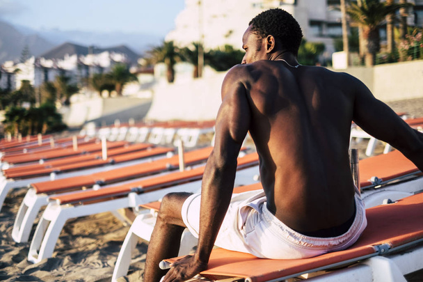 beautiful young black model man sit down on the seats at the beach. impressive body and muscle made with gym  and diet. nice lifestyle to gain the perfect body - Photo, Image