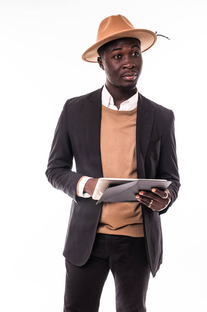 Jovem afro-americano bonito homem de negócios em terno e chapéu hipster usar tablet surf na internet ou verificar e-mails isolados em branco
 - Foto, Imagem