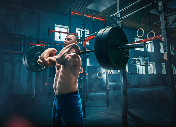 Fit young man lifting barbells working out in a gym - Foto, Bild