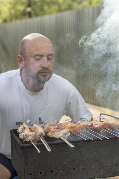 középkorú férfi élvezi a főzés a grill hús. szabadidő, élelmiszerek, emberek és ünnepek koncepció - boldog fiatalember főzés hús barbecue Grill szabadtéri nyári Party. - Fotó, kép
