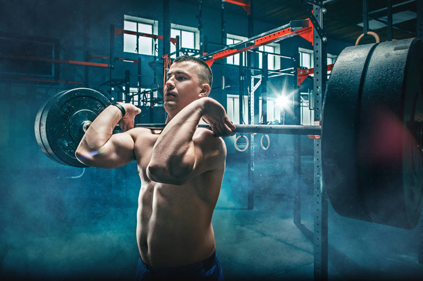 Fit young man lifting barbells working out in a gym - Fotoğraf, Görsel