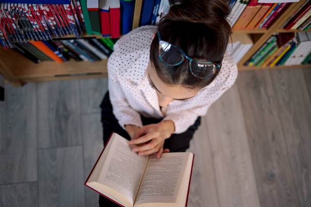 Όμορφη γυναίκα που φοράει γυαλιά, διαβάζοντας ένα βιβλίο στο κατάστημα βιβλίο. - Φωτογραφία, εικόνα