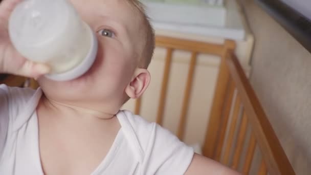 Two year old boy drinking milk from plastic bottle in his bed looking up - Imágenes, Vídeo