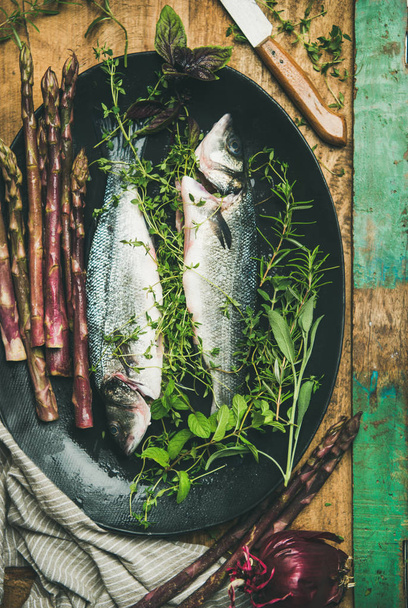 Cooking fish dinner. Raw uncooked sea bass with herbs and vegetables over rustic wooden background - Foto, Imagen