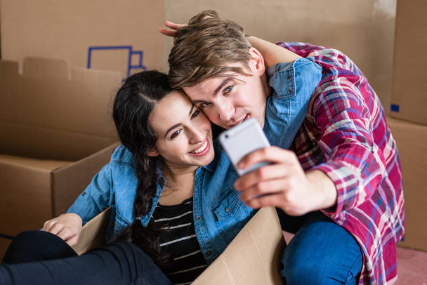 Feliz joven hombre y mujer haciendo una selfie después de mudarse juntos
 - Foto, imagen