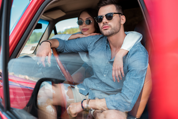 beautiful couple in sunglasses sitting in car and hugging together - Photo, Image