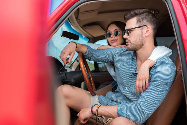young couple of travelers in sunglasses sitting in car and hugging together - Photo, Image
