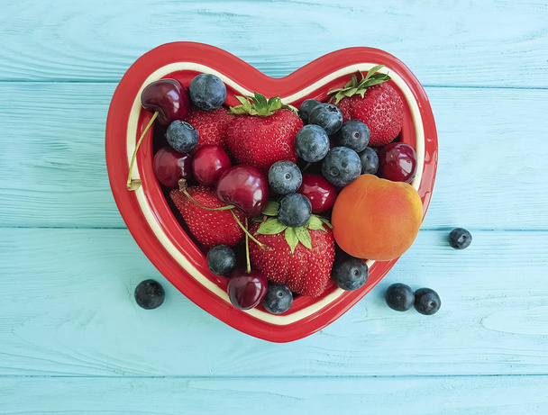fruit strawberry, blueberry, cherry, apricot plate heart on blue wooden - Fotó, kép