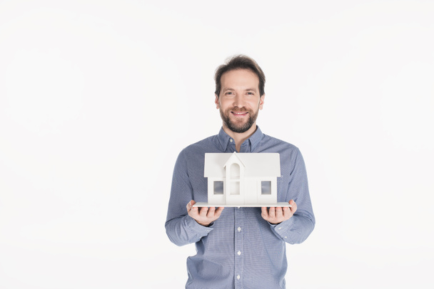 портрет веселого бородатого мужчины, держащего модель дома в руках, изолированных на белом
 - Фото, изображение