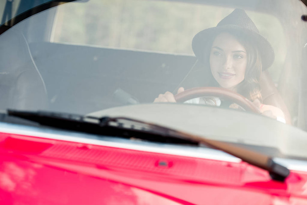 beautiful young woman in hat driving car during road trip - Foto, Bild