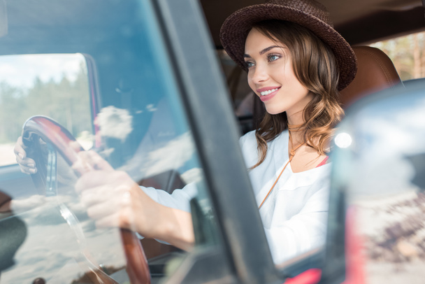 happy beautiful young woman in hat driving car during road trip - Фото, изображение