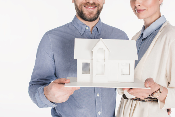 visão parcial de casal sorridente com modelo de casa isolado em branco
 - Foto, Imagem