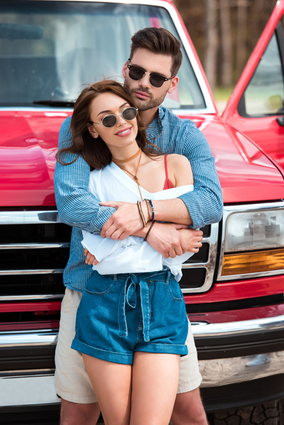 smiling beautiful couple embracing near red jeep  - 写真・画像
