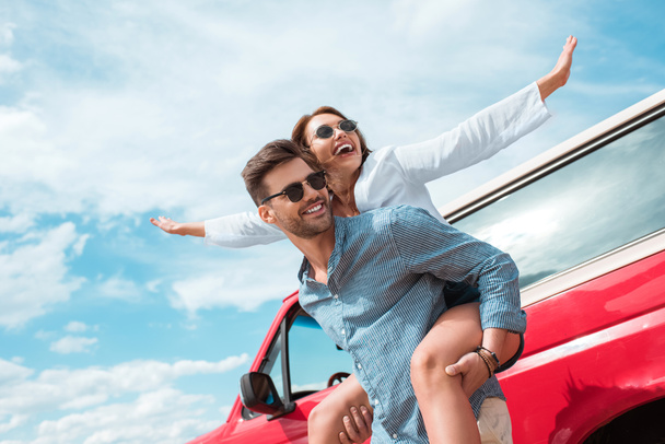 excited young couple of travelers piggybacking at car - Photo, Image