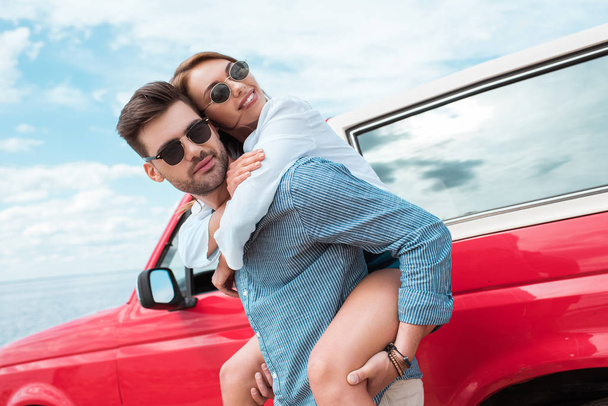 heureux jeune couple de voyageurs piggybackking près de voiture rouge
  - Photo, image