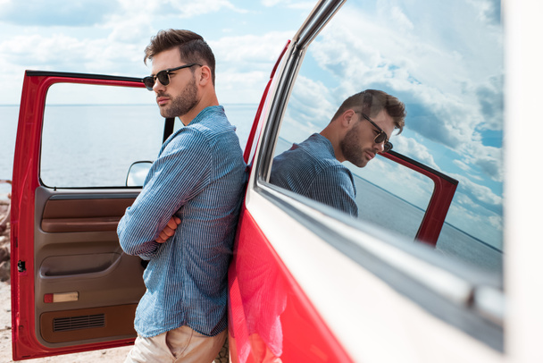 handsome stylish male traveler in sunglasses posing at red car near the sea - Foto, Bild