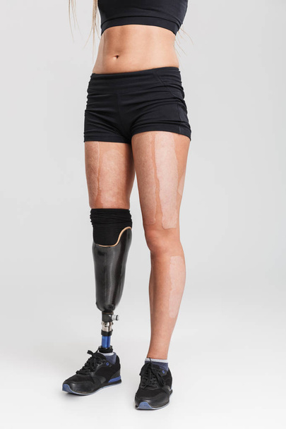Cropped image of a healthy young disabled sportswoman standing isolated over grey background - Fotó, kép
