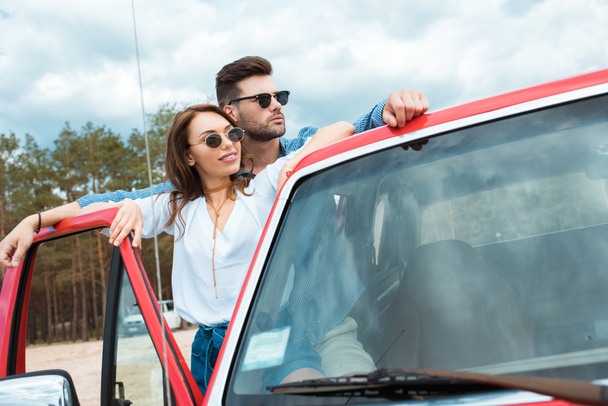 couple of travelers in sunglasses standing near red car - 写真・画像