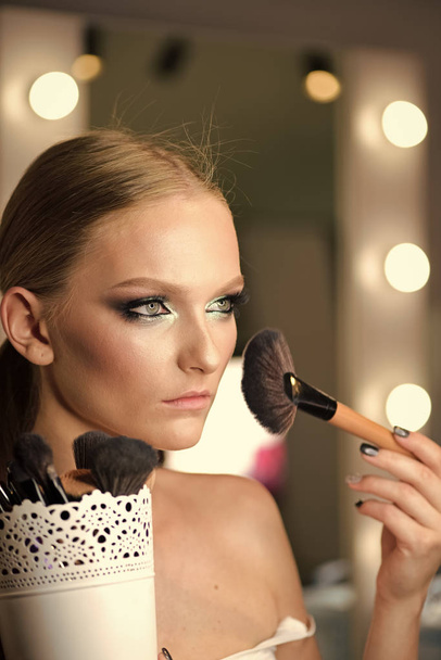 Beautiful young woman applying foundation powder or blush with makeup brush - 写真・画像