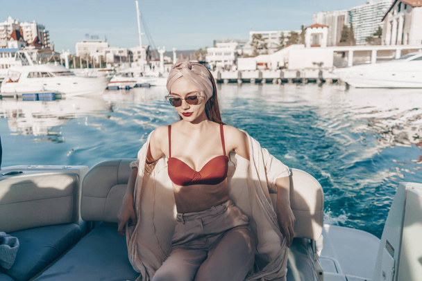 a luxurious attractive girl in sunglasses enjoys relaxing on her white yacht, a long-awaited vacation - Foto, imagen