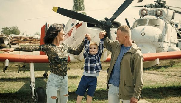 Child Childhood Children Happiness Concept. Happy family spend time together, on excursion, helicopter or plane on background, sunny day. Mother and father and their child walking in aviation museum - Photo, image