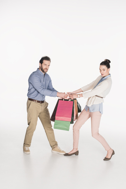 side view of couple looking at camera while pulling over shopping bags isolated on white - Photo, Image
