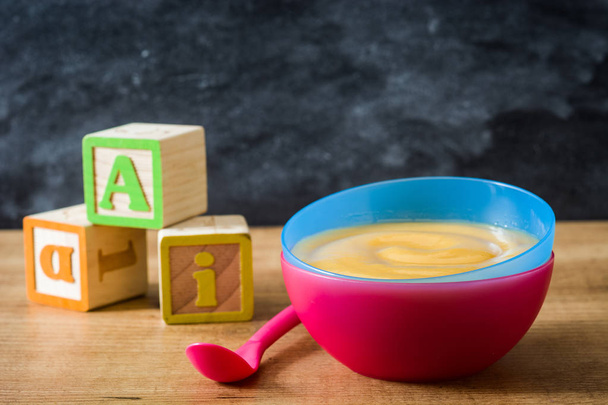 Alimenti per bambini: ciotola colorata di purea di frutta su tavolo di legno
 - Foto, immagini