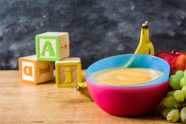 Alimenti per bambini: ciotola colorata di purea di frutta su tavolo di legno
 - Foto, immagini