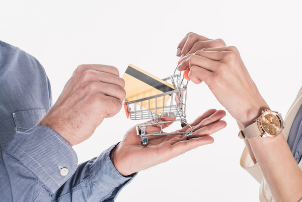 cropped shot of couple holding little shopping cart and credit card in hands isolated on white - Photo, Image