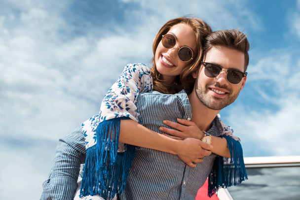 homem bonito em óculos de sol piggybacking sua namorada sorridente
 - Foto, Imagem