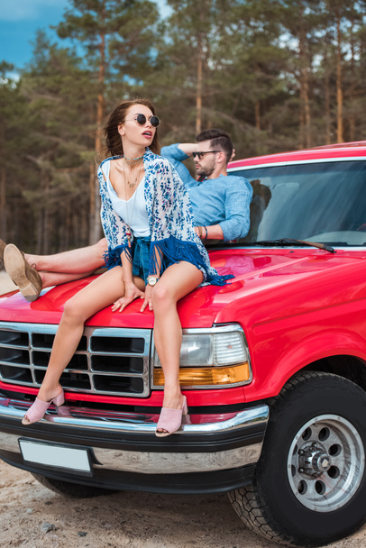 όμορφο κομψό ζευγάρι κάθεται στο κόκκινο αυτοκίνητο για το σαββατοκύριακο - Φωτογραφία, εικόνα