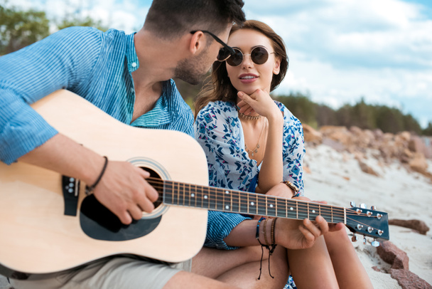 male guitarist playing acoustic guitar and sitting with girlfriend outdoors - Zdjęcie, obraz