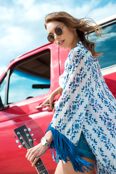 attractive young woman with acoustic guitar posing near red car - Photo, Image