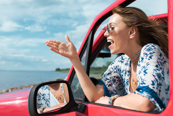 Fröhliche junge Frau gestikuliert und redet während der Fahrt im Auto - Foto, Bild