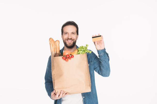 портрет улыбающегося мужчины с кредитной картой и бумажной упаковкой, полной еды, изолированной на белом
 - Фото, изображение