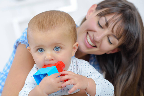 Mother smiling at baby chewing toy - Фото, изображение