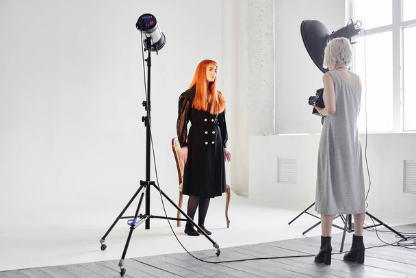 Girl photographer photographing fashion model in black color on white background in Studio - Valokuva, kuva