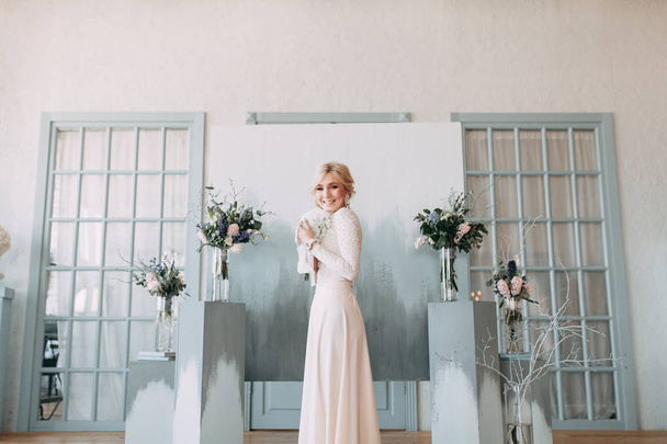 Beautiful bride in front of wedding arch with flowers and decor. Bouquet in the hands and details. The girl is happy, smiling and dancing. Dream wedding dress in modern style - Photo, image