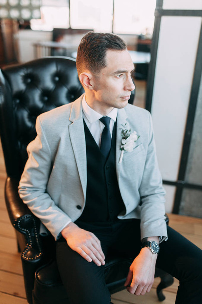 Gathering of a beautiful groom, waiting for the bride. Photo shoot in the interior Studio. Wedding in European style. Handsome man in a jacket and trousers - Фото, изображение