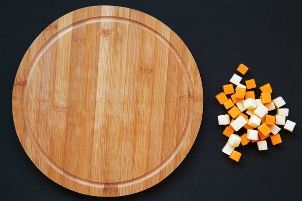 Edam and mimolette cheese with round bamboo board on dark background. Copy space, top view. Flat lay. - Photo, Image