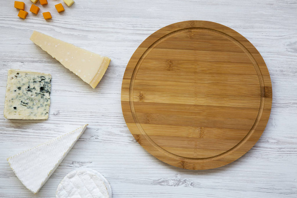 Delicious cheeses with round bamboo board on a white wooden background, top view. From above, flat lay. - Photo, Image