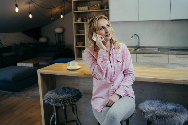 Beautiful young woman freelancer works in an apartment with phone and notebook. Business concept - Valokuva, kuva