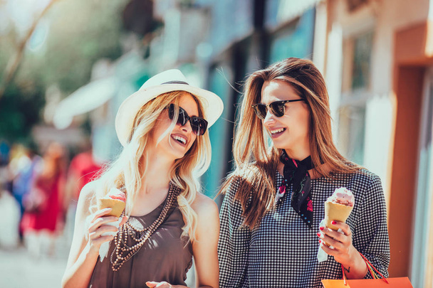 Happy young women with shopping bags and ice cream having fun on city street - Фото, изображение