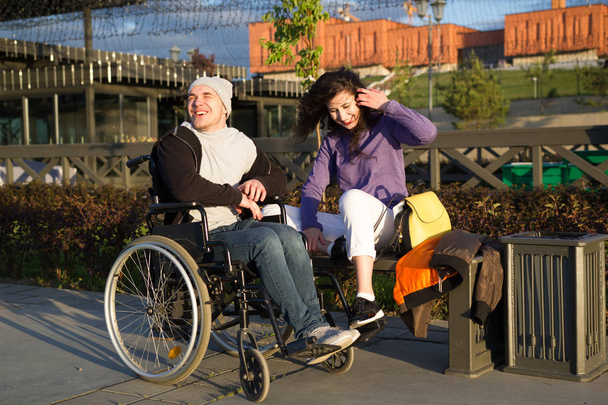 Couple heureux - homme handicapé en fauteuil roulant parlant avec une jeune femme attrayante profitant du coucher du soleil
 - Photo, image